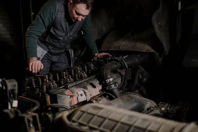 A mechanic leaning over the exposed diesel engine of a truck in a repair shop.