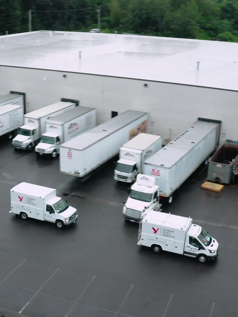 Two Patriot Fleet Services mobile shops pulling into a customer's yard, seen from above, with a line of trailers backed up to the loading docks behind them.